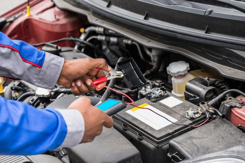 A Man is Working on a Car Battery With a Pair of Pliers — C & K Maintenance In Kawana, QLD