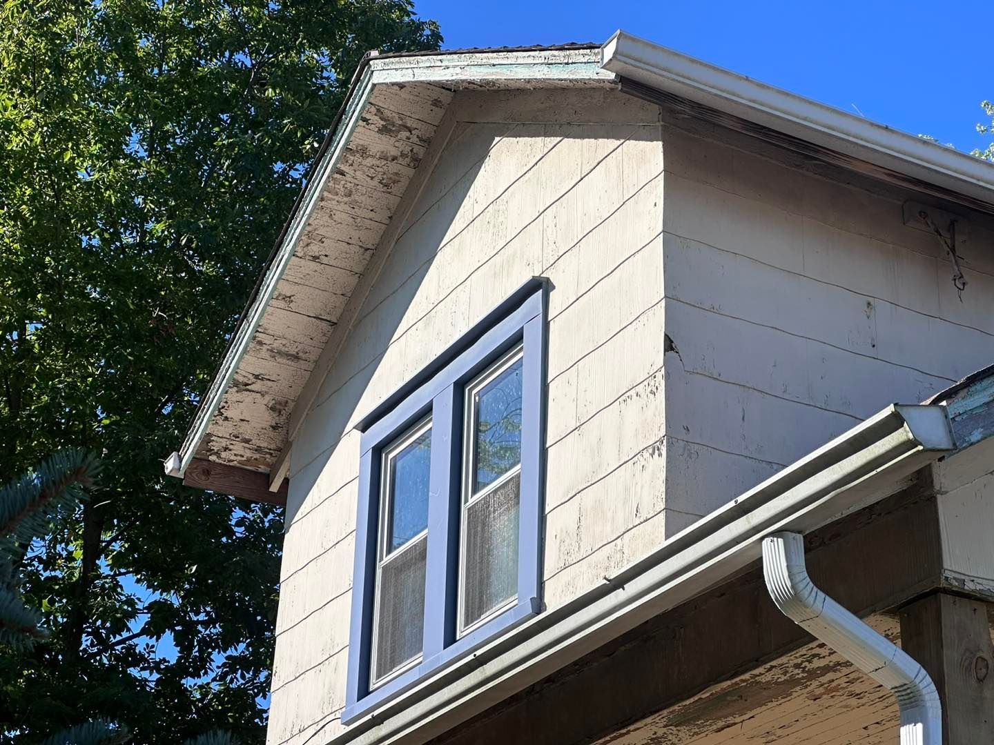 A white house with a blue window and a white gutter