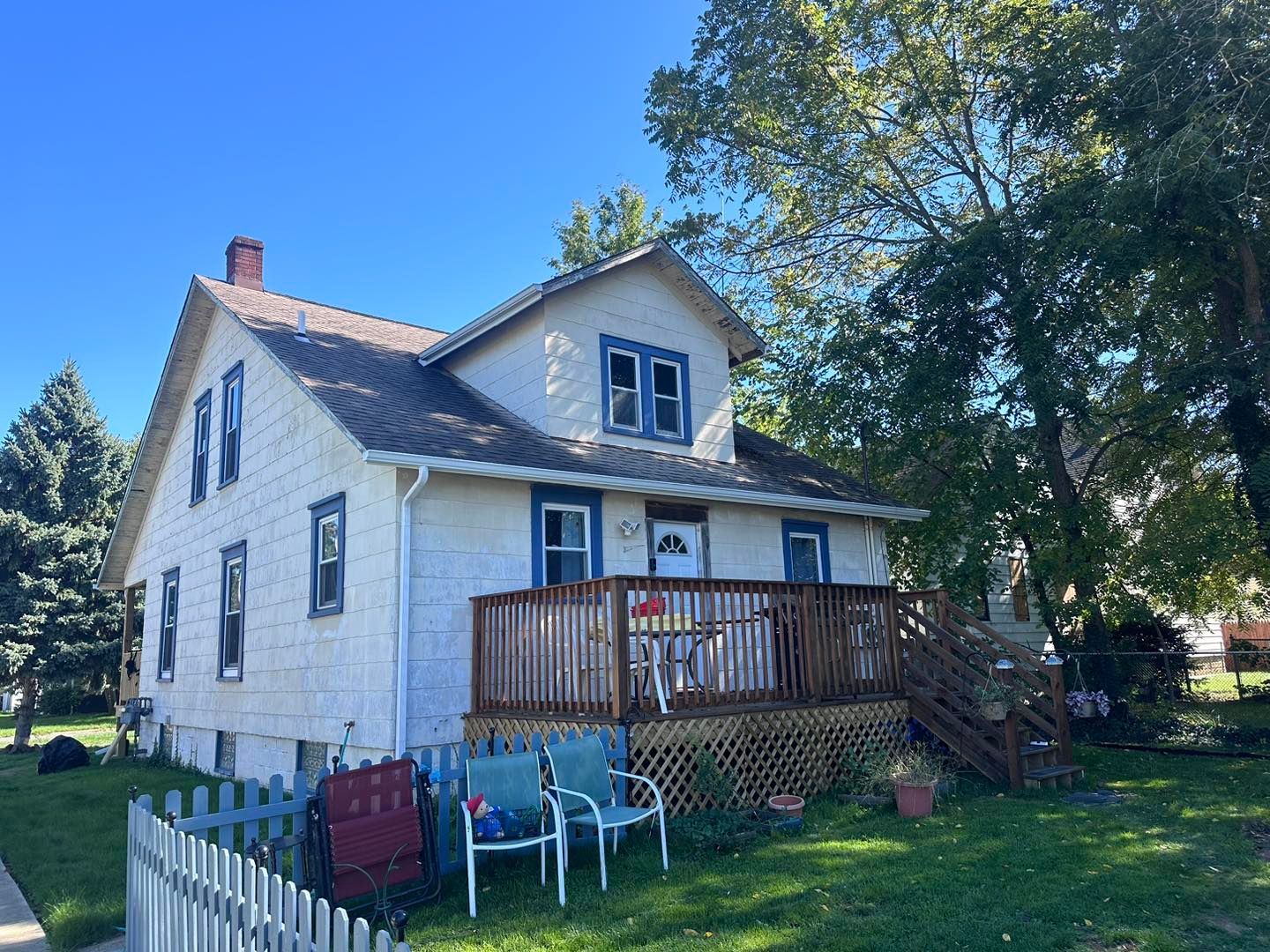 A white house with a deck and chairs in front of it.