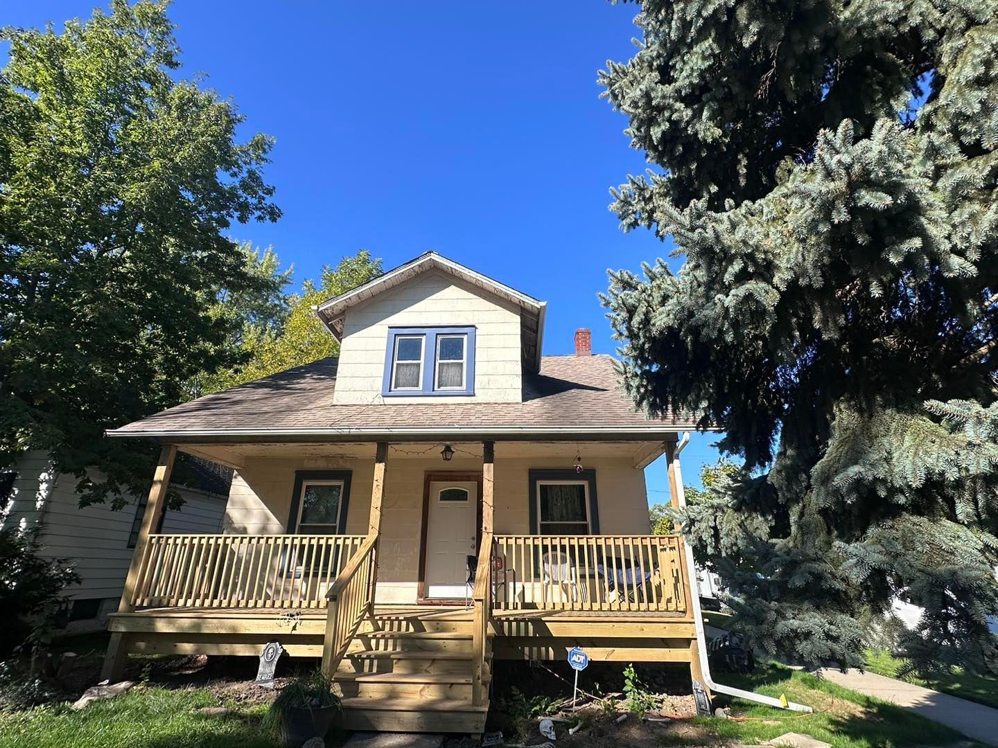 A house with a porch and a large tree in front of it.