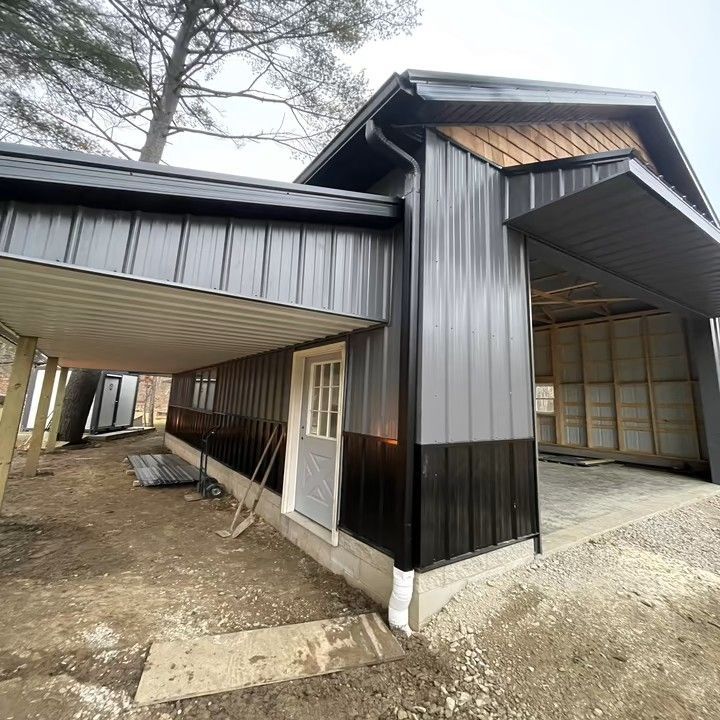 Modern barn-style building with black and gray metal siding, a carport, and an open garage entrance.