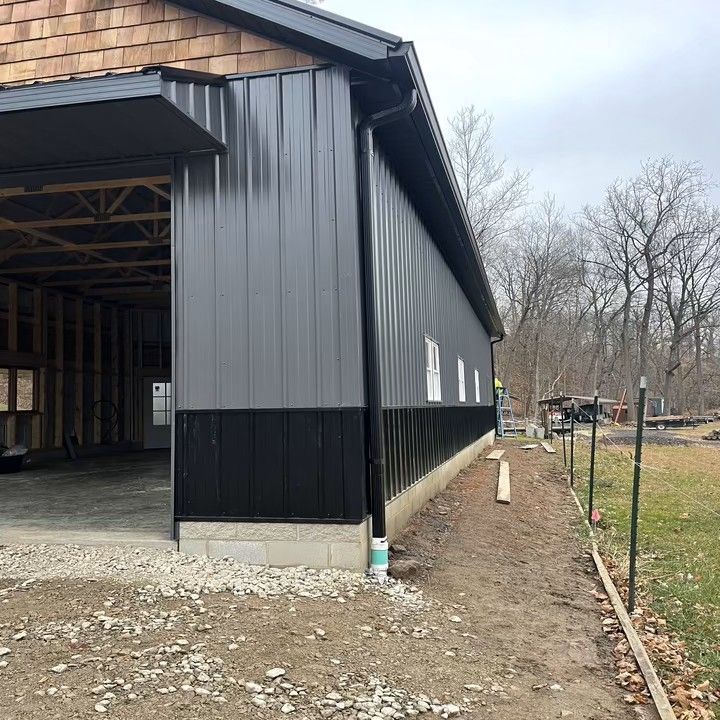 Dark gray and black metal building with an open garage door and a gravel driveway.