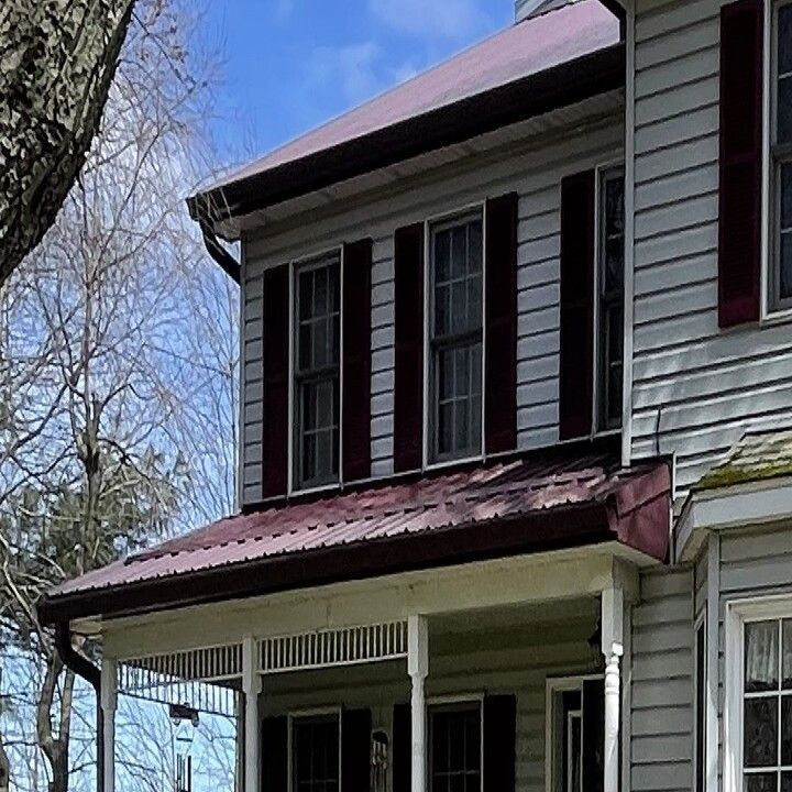 Two-story house with gray siding, burgundy shutters, and a burgundy metal roof. A porch is in the front.