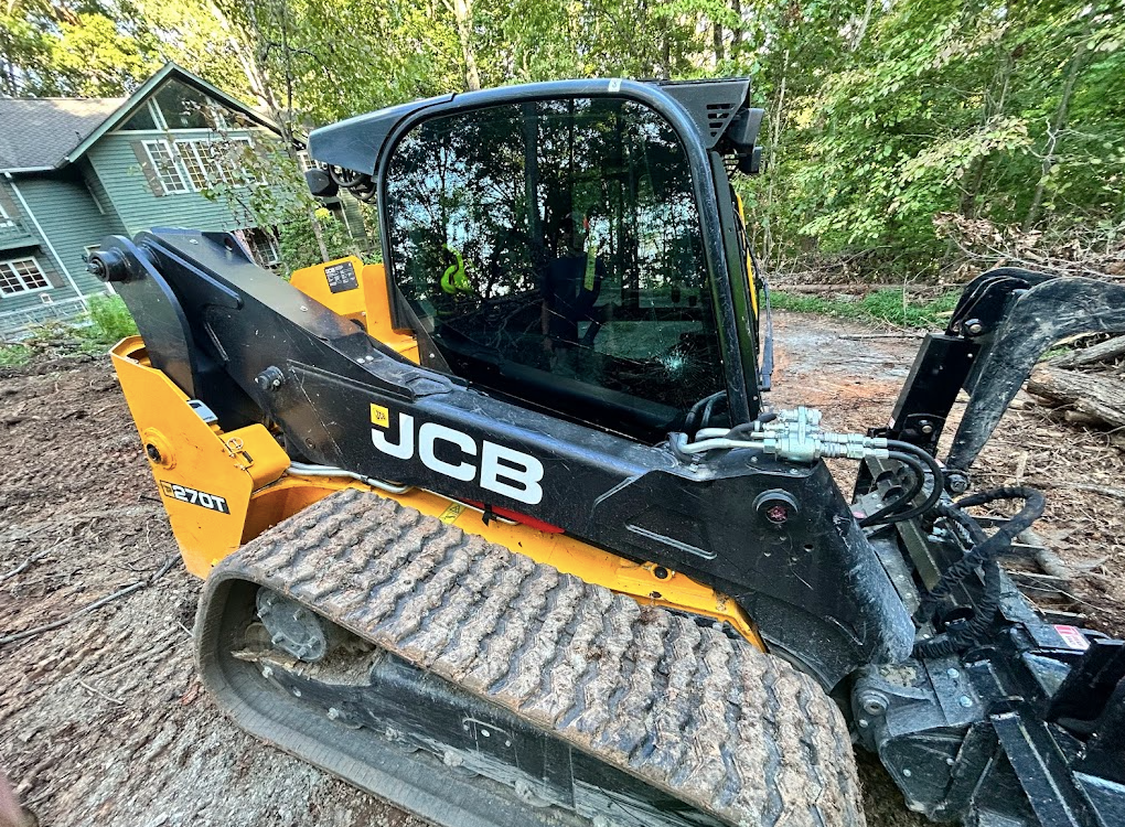 A jcb bulldozer is parked in a dirt field in front of a house.