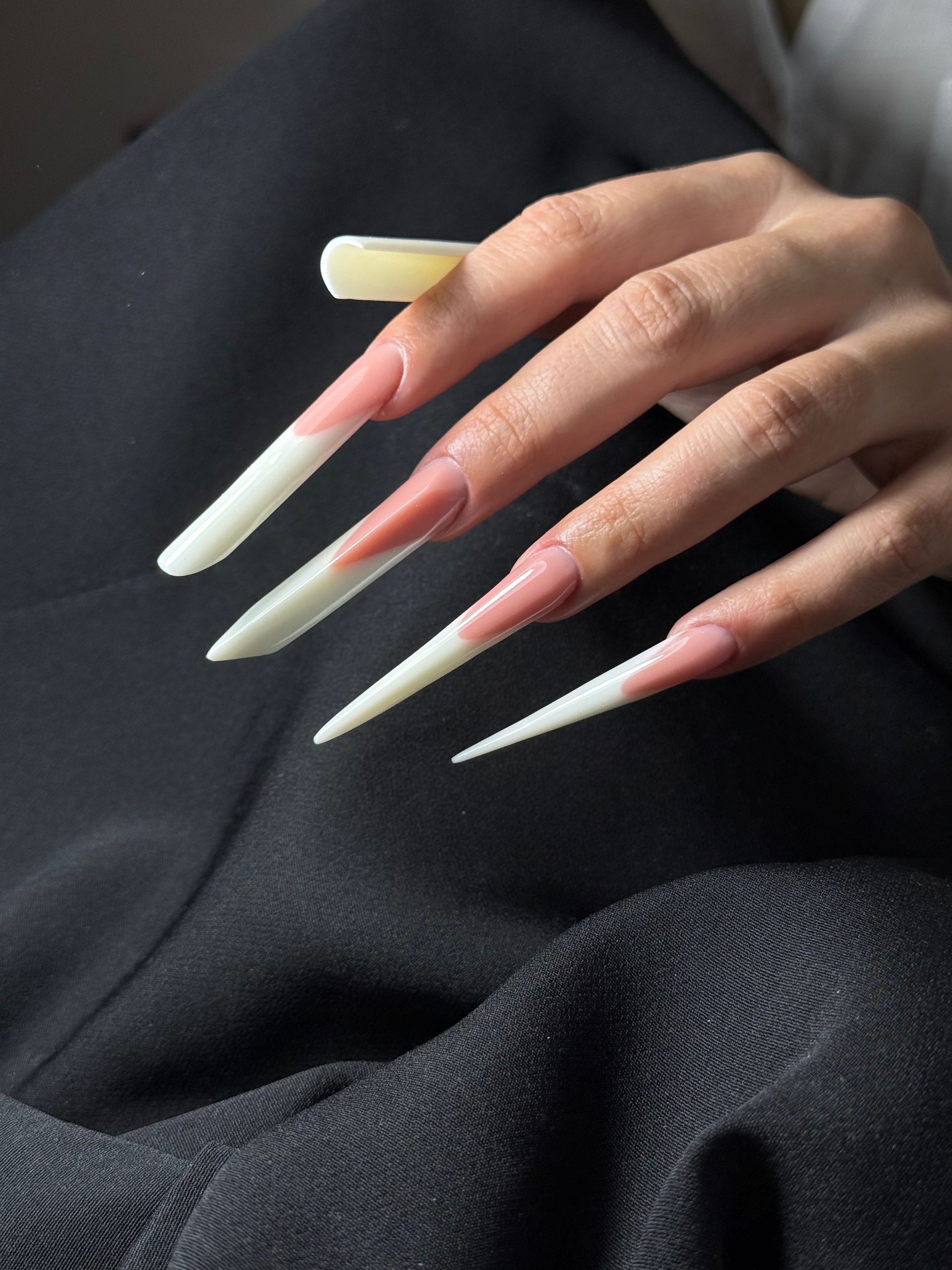 Hand with long, pink and white french tip coffin-shaped nails. One nail has a lavender tip.