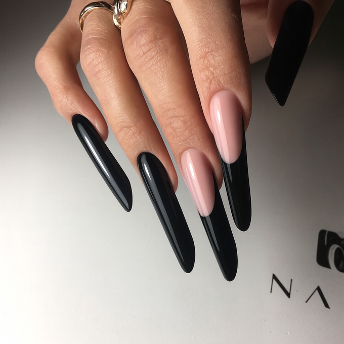 Hand with long, black and nude-colored coffin-shaped nails, on a white surface.