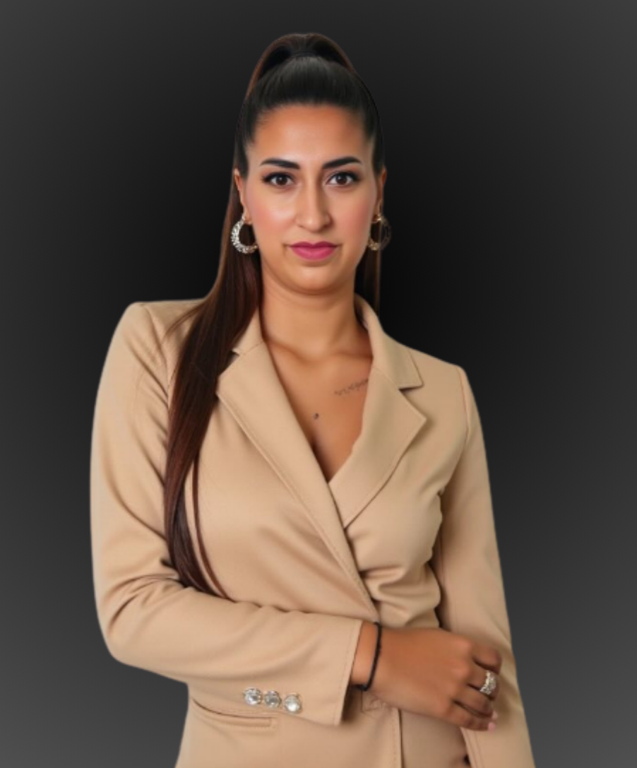 Woman with long brown hair in a tan blazer, looking at the camera. Black background.