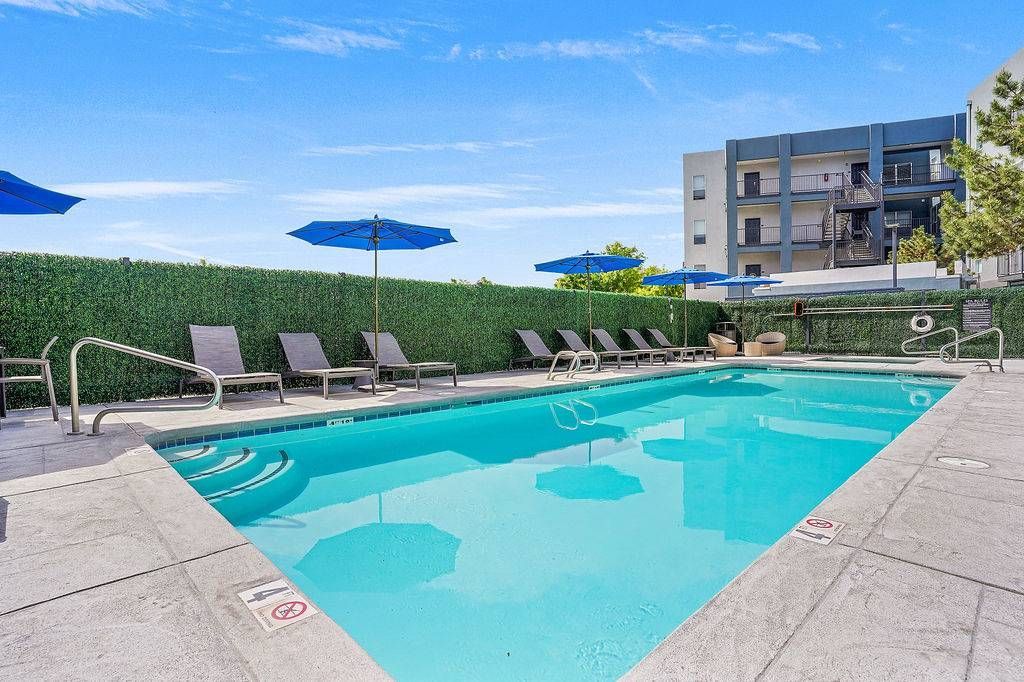Outdoor pool area with lounge chairs and blue umbrellas at an apartment community.