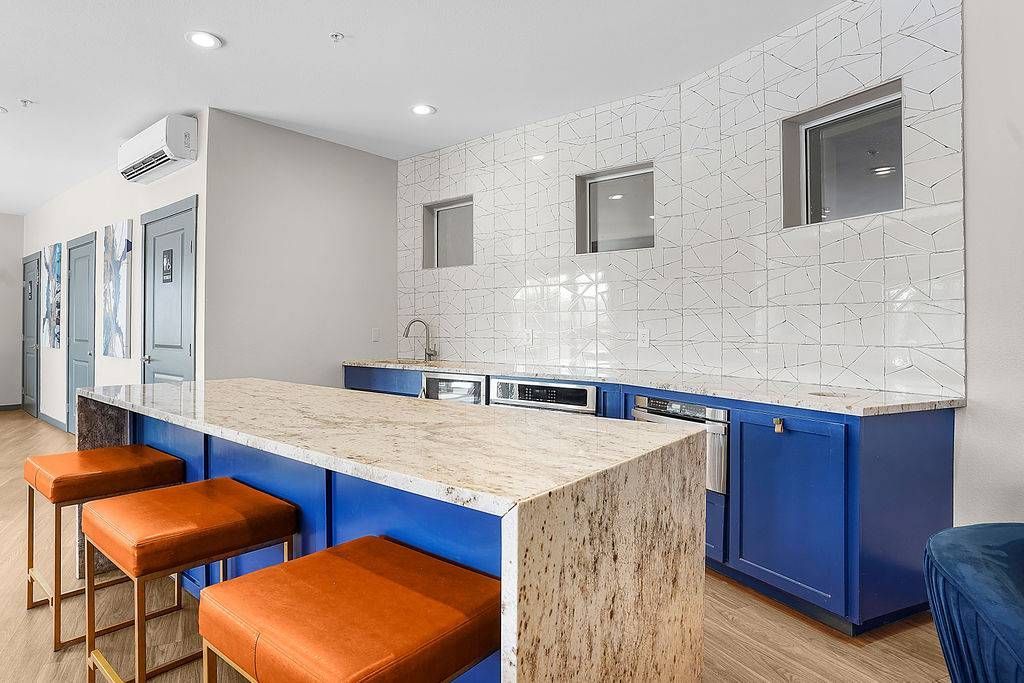 Modern communal kitchenette with marble island, blue cabinets, and orange bar stools.