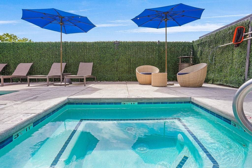Outdoor pool area with blue umbrellas, lounge chairs, and wicker seating on a sunlit patio.