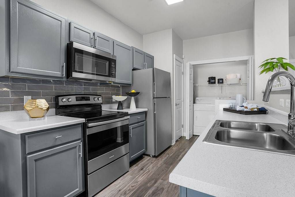 Modern apartment kitchen with gray cabinets, stainless steel appliances, and a double sink.