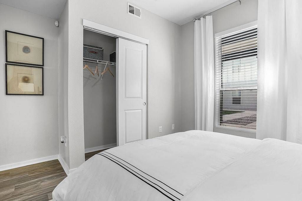 Bedroom with a white bed, open closet, and window with blinds.