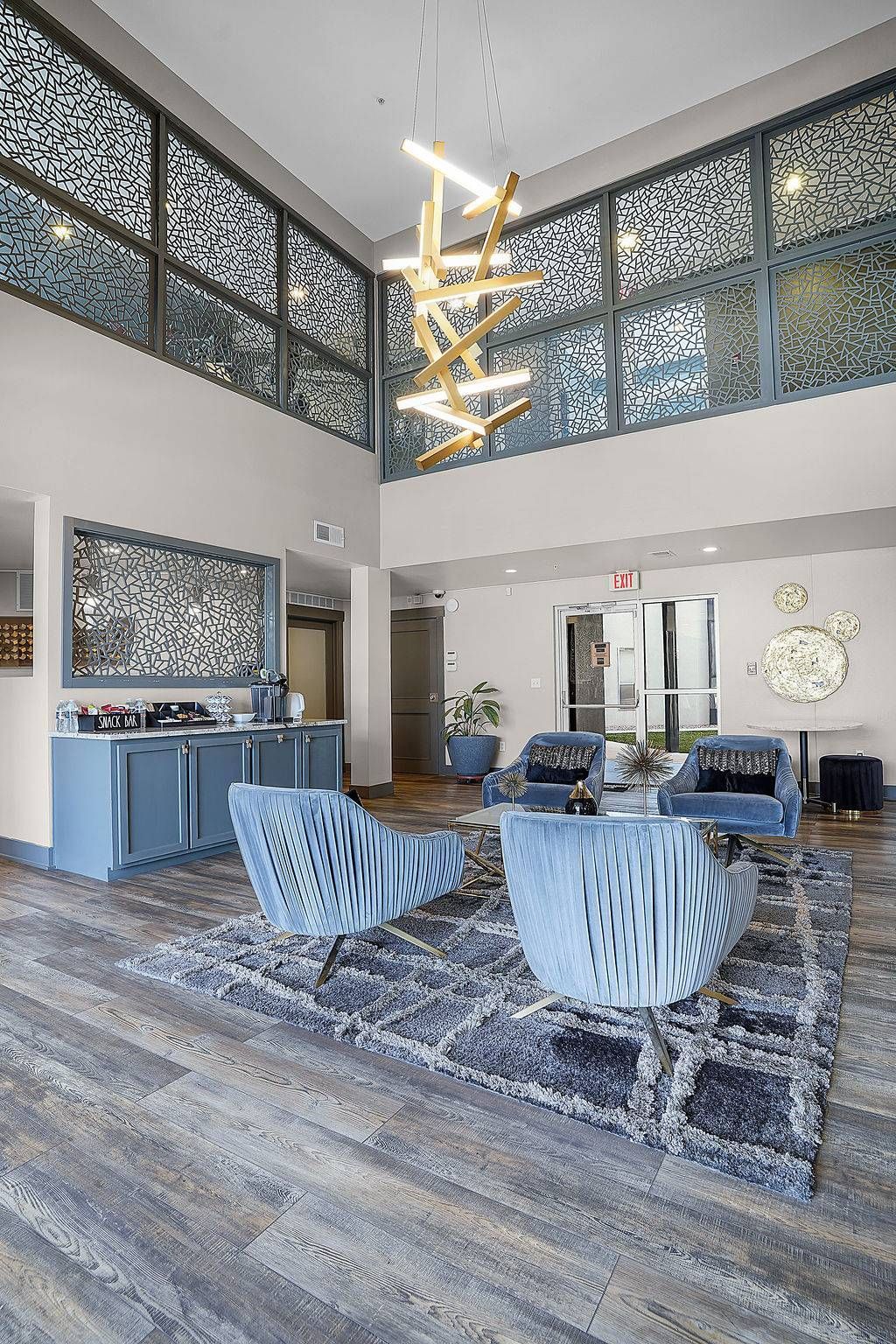 Modern apartment lobby with blue lounge seating, decorative screens, and a chandelier.