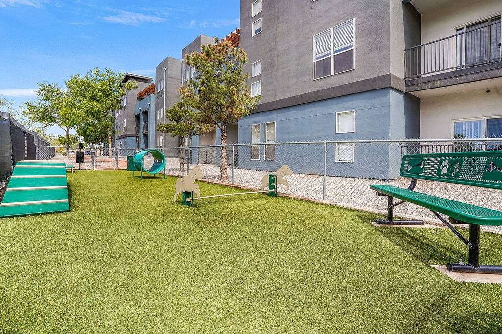 Community outdoor amenity with turf, fencing, benches, and play equipment beside an apartment building.