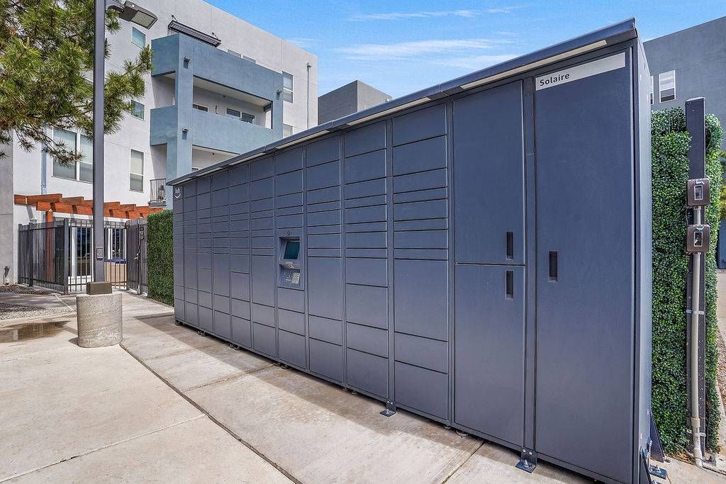 Exterior view of a long row of gray, external package lockers beside an apartment building.