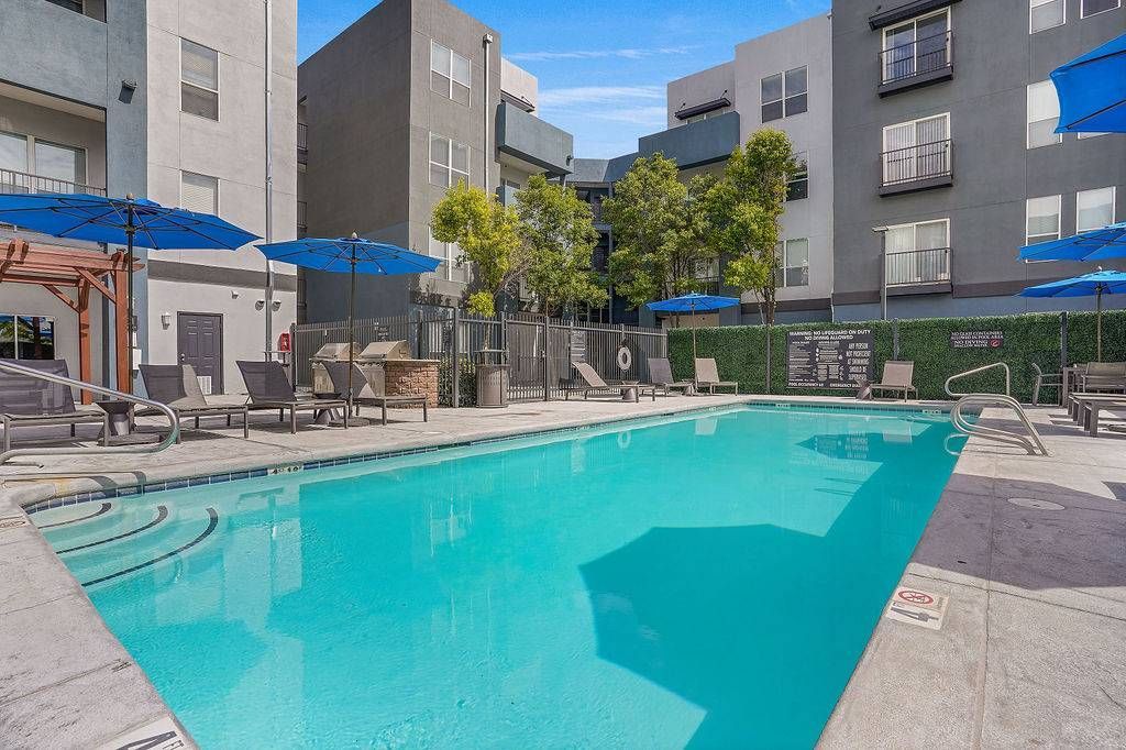 Outdoor apartment pool with lounge chairs and blue umbrellas.