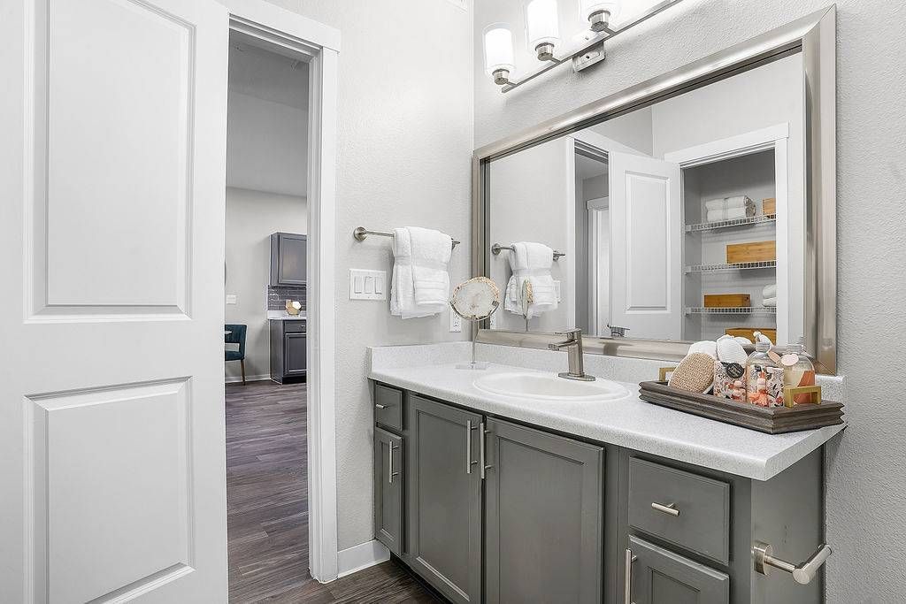 Bathroom vanity with sink, large mirror, and organized cabinet with towels.