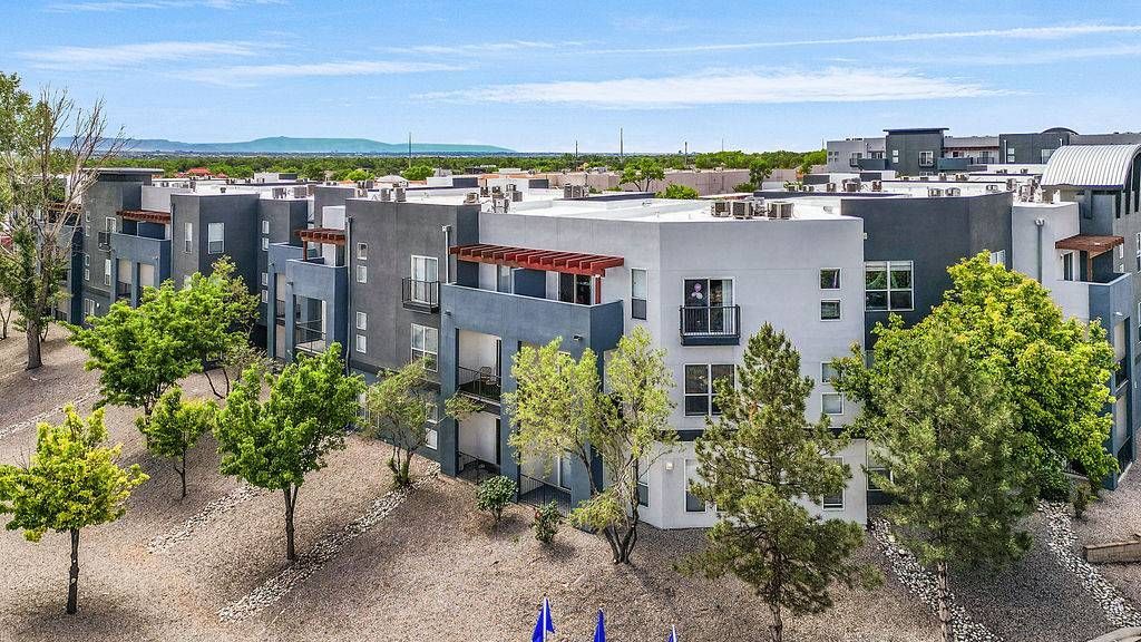 Aerial view of a modern apartment complex with white and gray buildings, balconies, and trees.