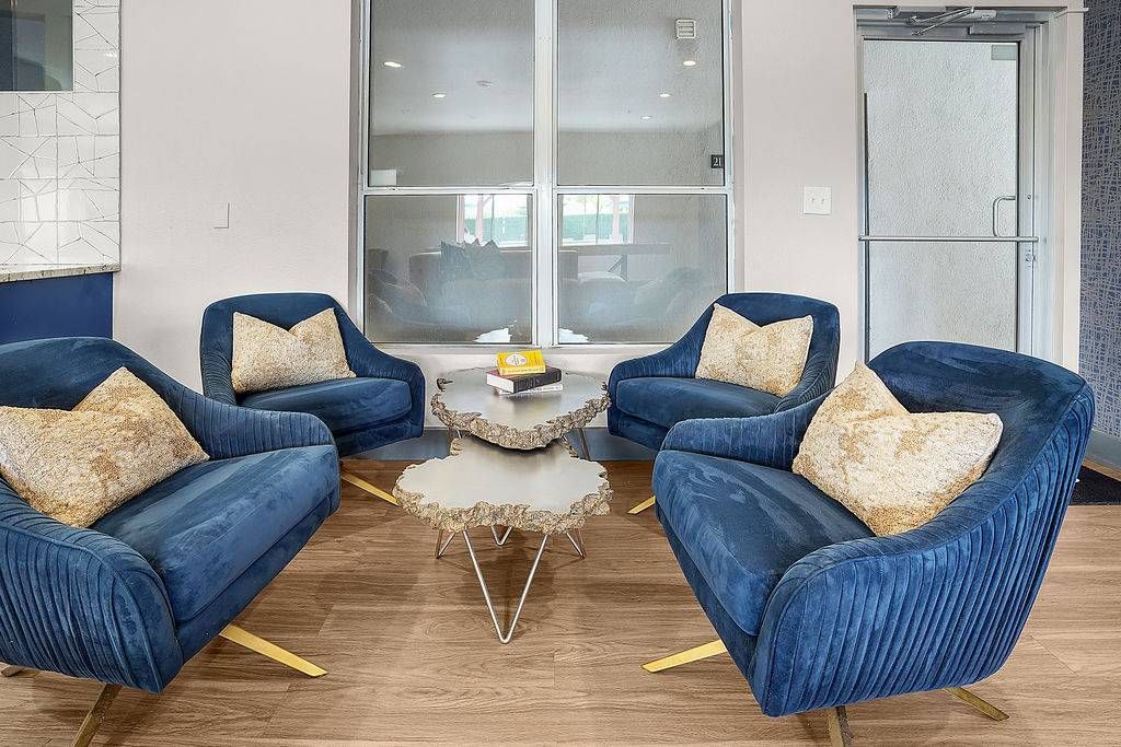 Four blue velvet lounge chairs arranged around a sculptural coffee table in a modern apartment community lounge.