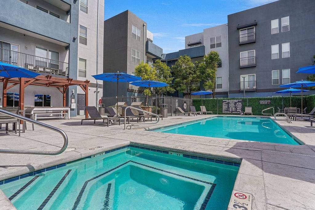 Outdoor community pool and hot tub area with blue umbrellas and lounge chairs.