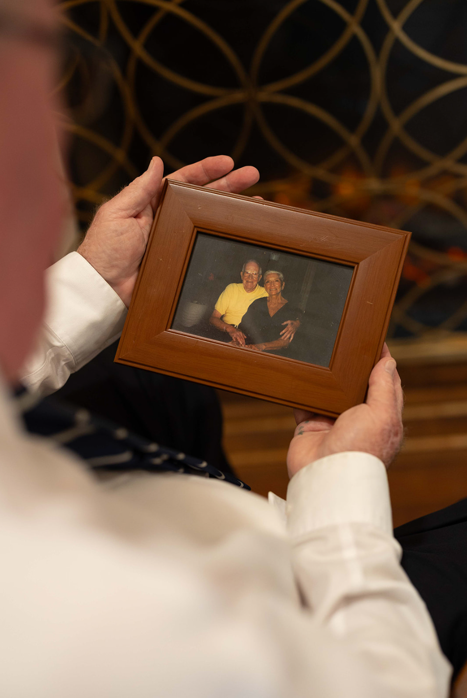 Person holding a framed photograph of two people smiling, indoor setting.