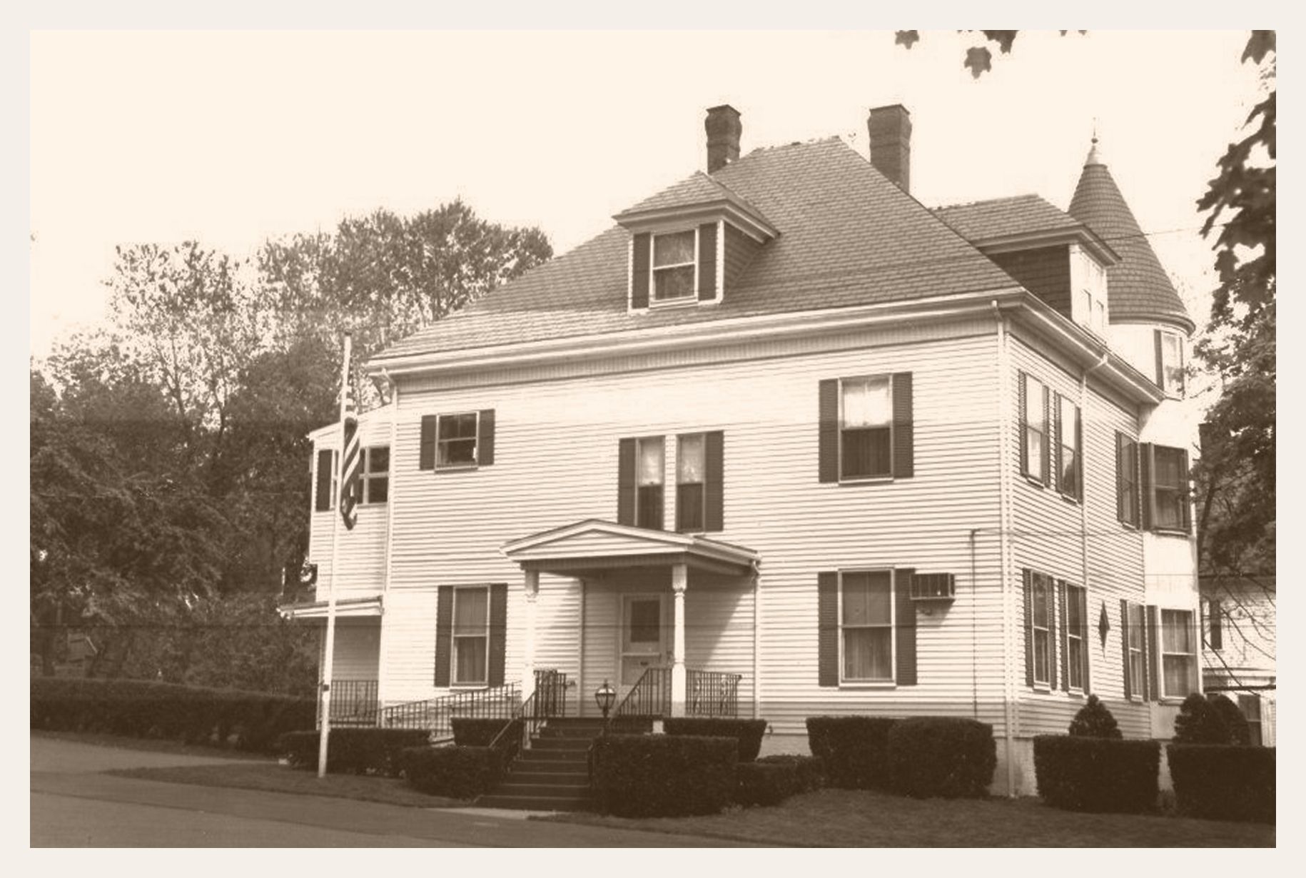 A white, two-story house with black shutters, a porch, and a wooden fence. Trees flank the house.