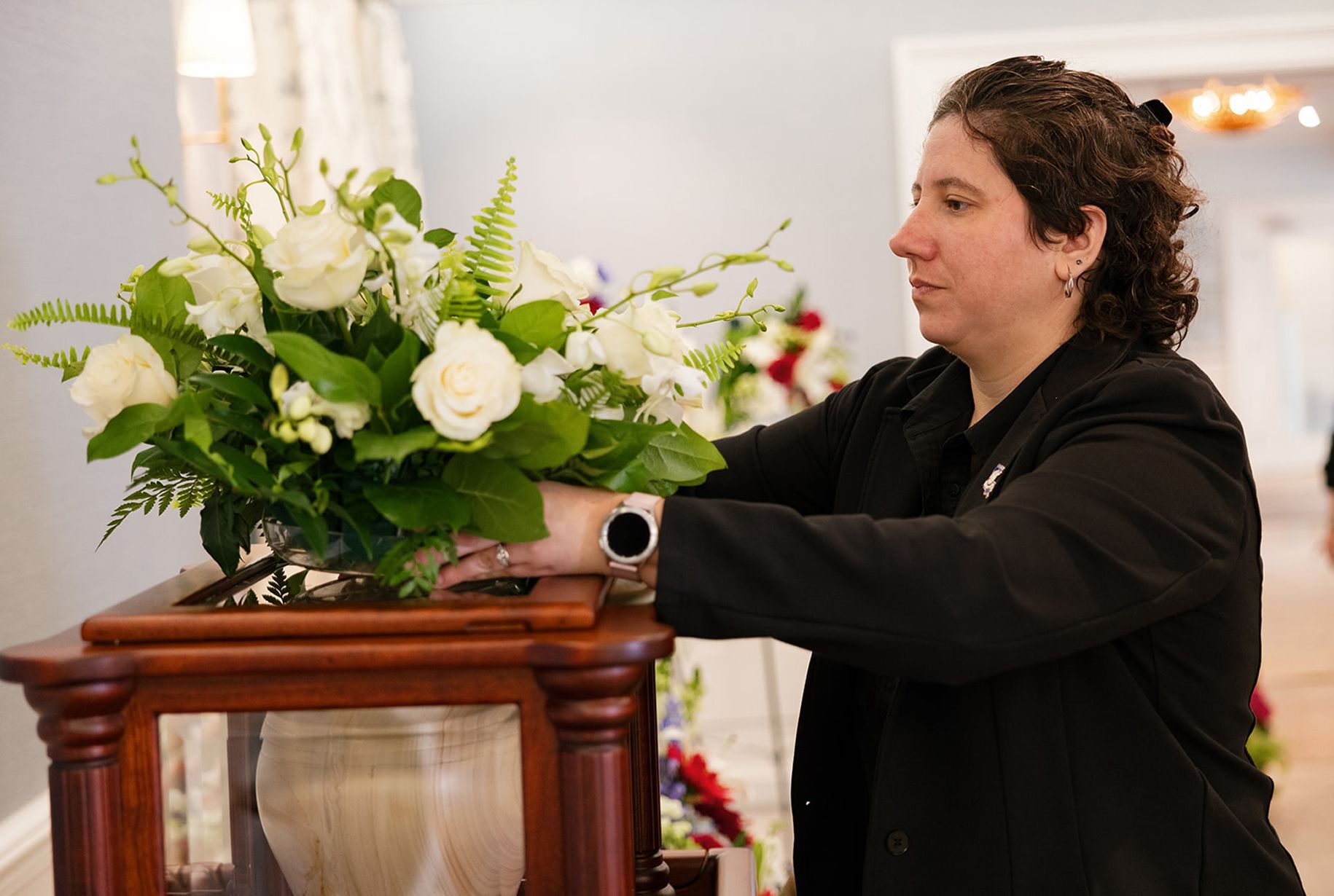 Woman places white flower arrangement on wooden cabinet with glass front.