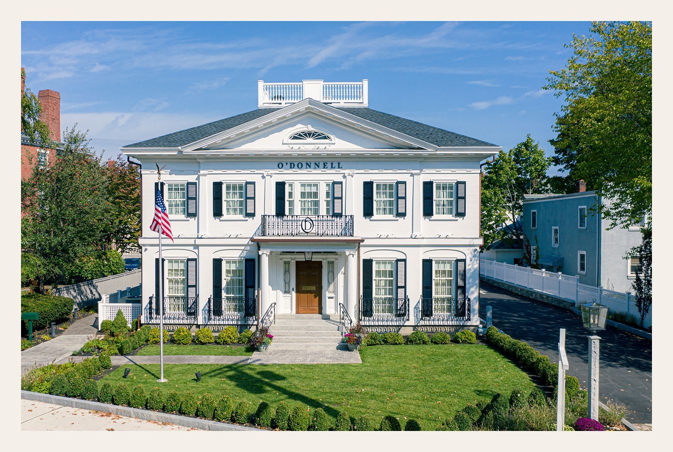 White two-story building with black shutters, American flag, and manicured lawn.