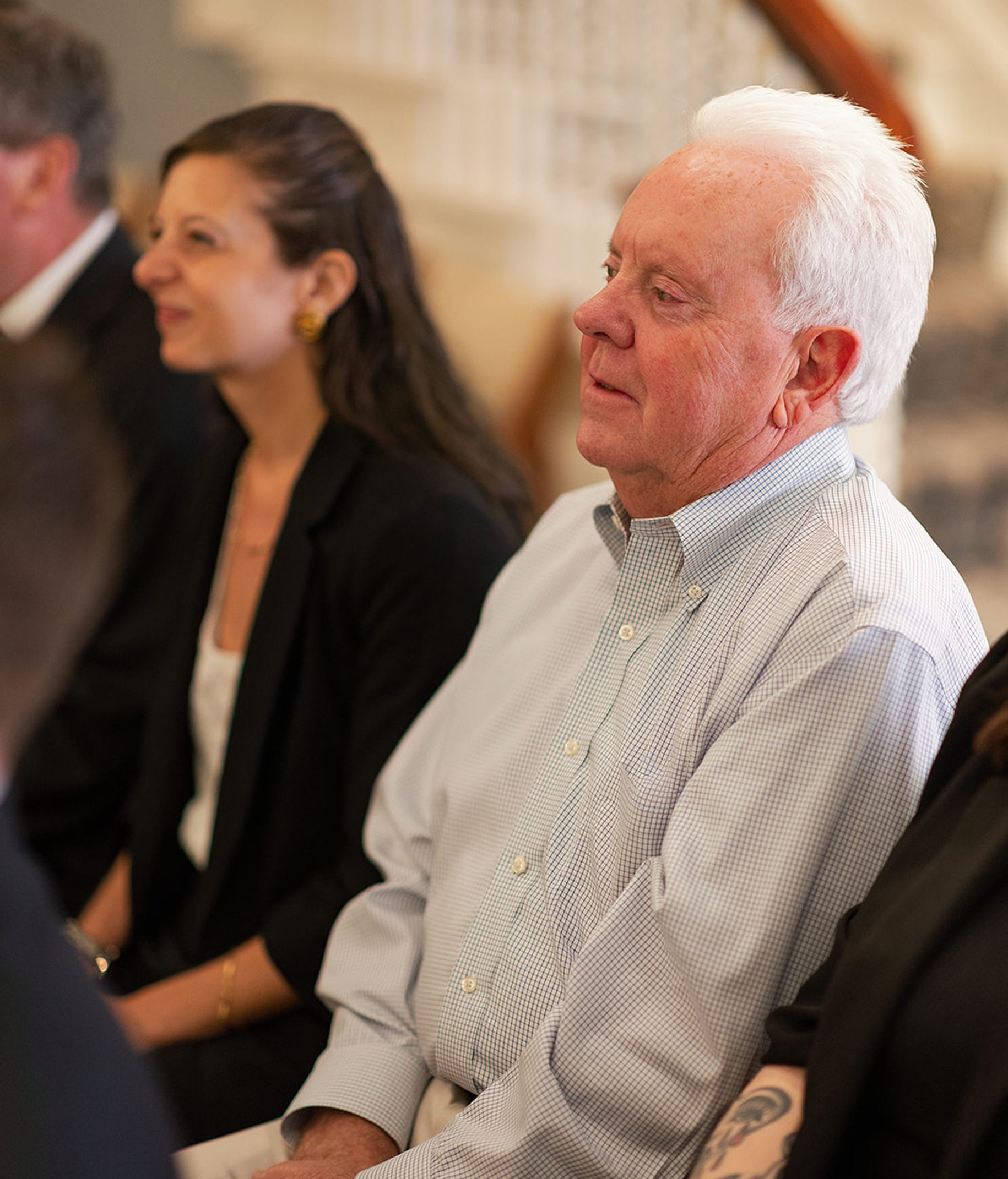 Man in light blue shirt sits next to woman in black blazer; both seated indoors.