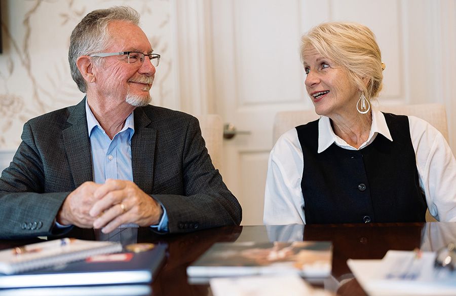 Two people, seated at a table, looking at each other, smiling.