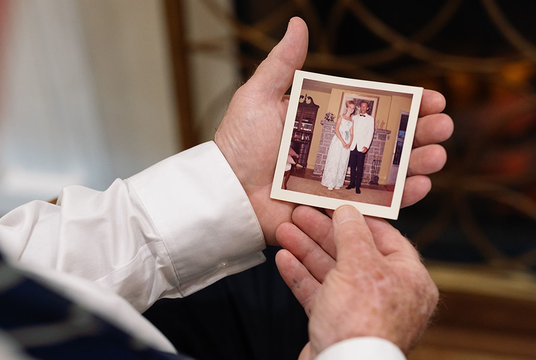 Hands holding a faded photograph of a couple in wedding attire.