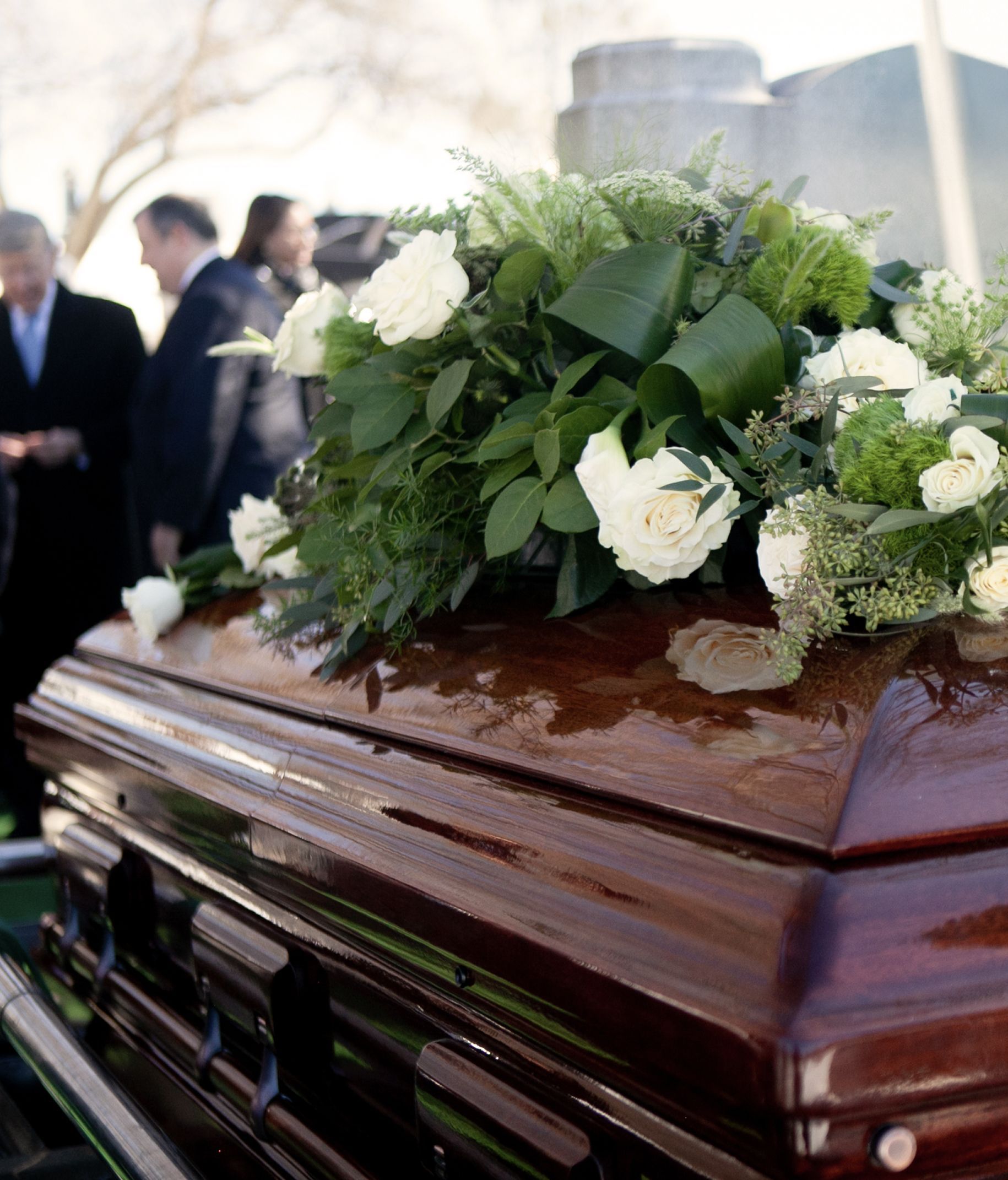 Wooden casket with floral arrangement; people in background.