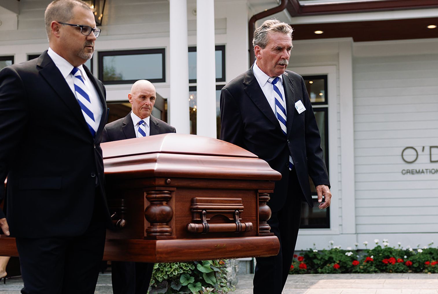 Men in suits carry a casket outside a funeral home.