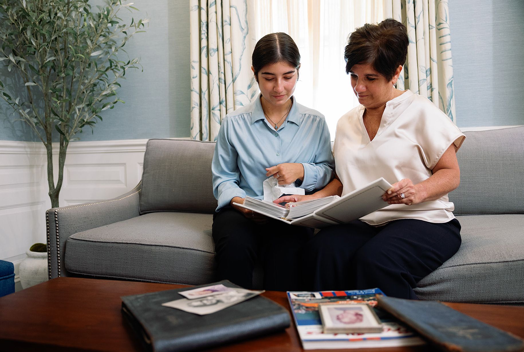 Two people looking at a photo album together on a couch, with a coffee table in front of them.