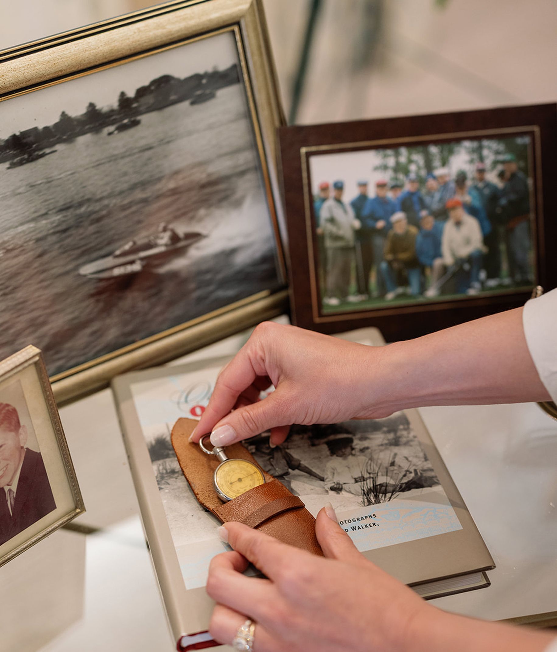 Hands holding a key near a leather case on top of a book and framed photos.