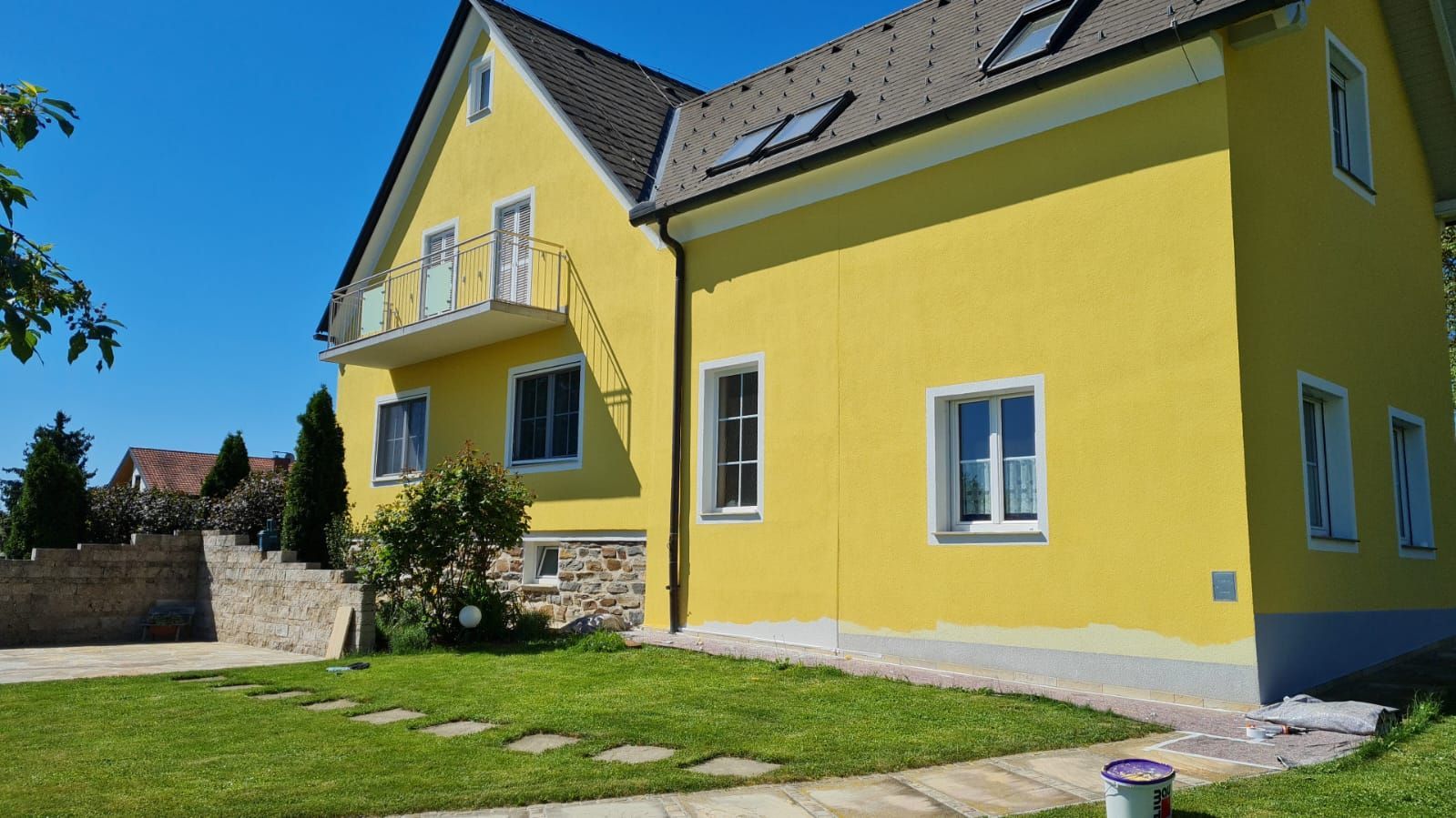 Ein gelbes Haus mit grauem Dach wird gestrichen.