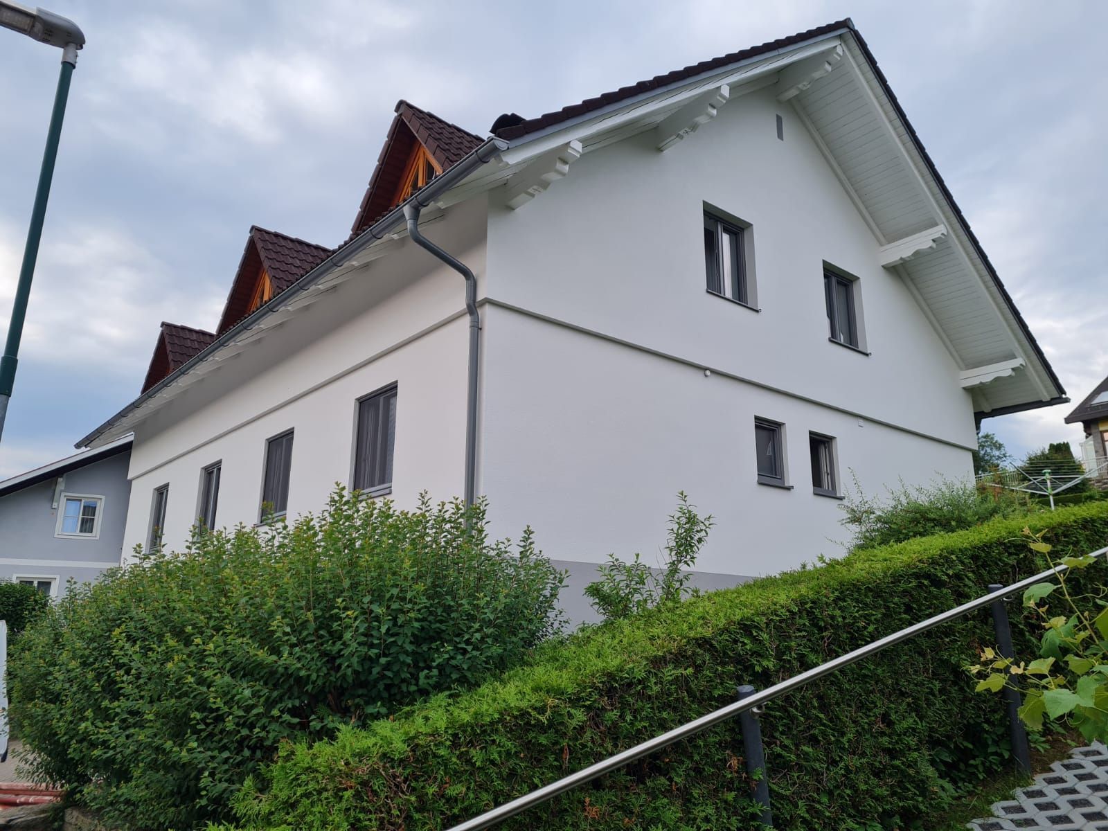 Ein weißes Haus mit rotem Dach ist von grünen Büschen umgeben