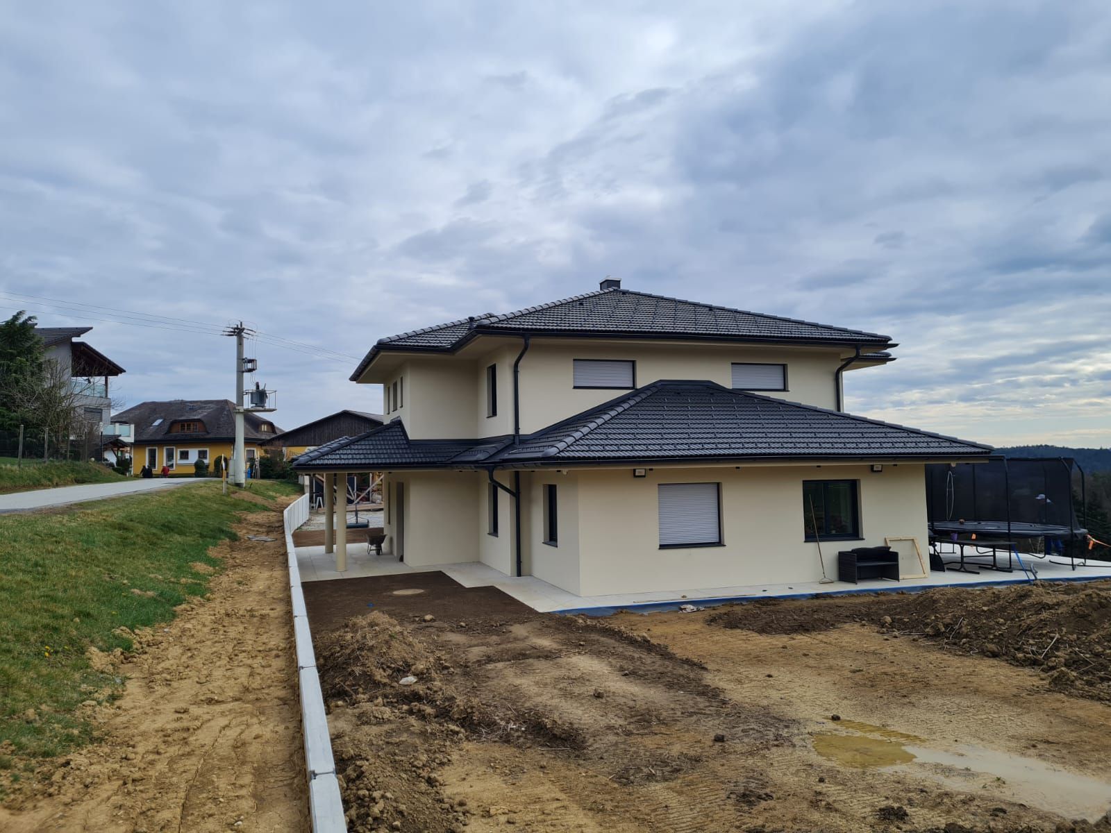 Auf einem Erdhügel steht ein großes weißes Haus mit schwarzem Dach.