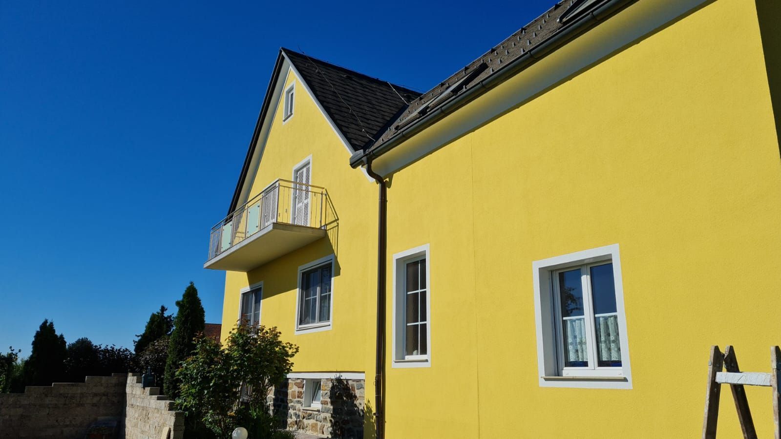 Ein gelbes Haus mit einem Balkon und einer Leiter davor.