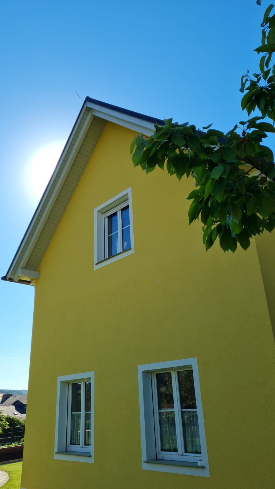Ein gelbes Haus mit weißen Fenstern und einem Baum davor.