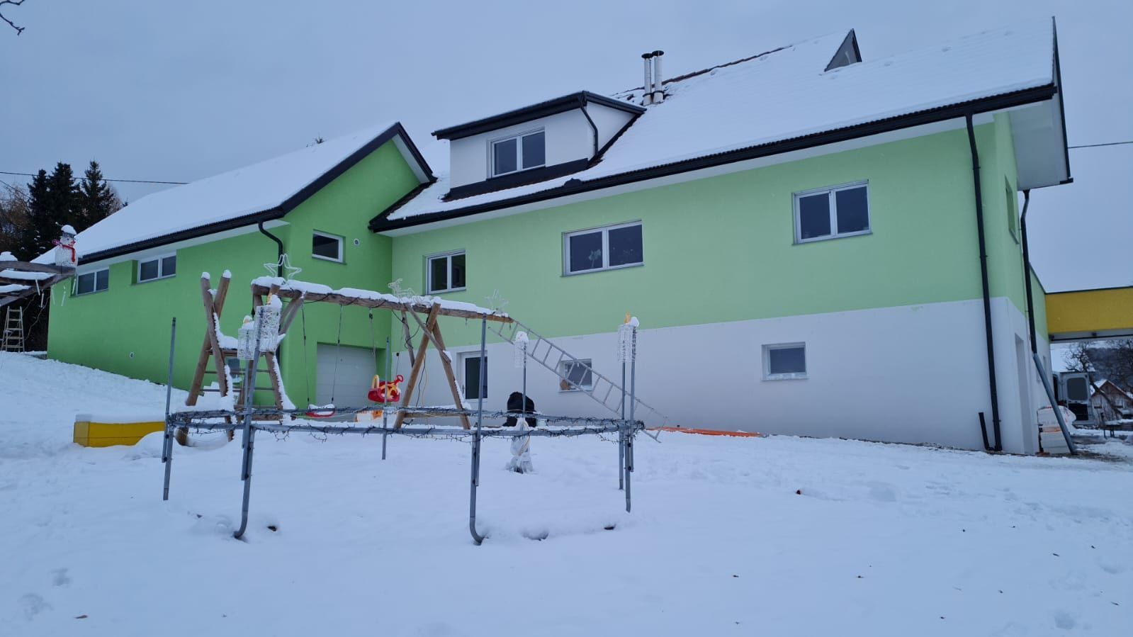 Ein grünes Haus mit einer Schaukel davor im Schnee.