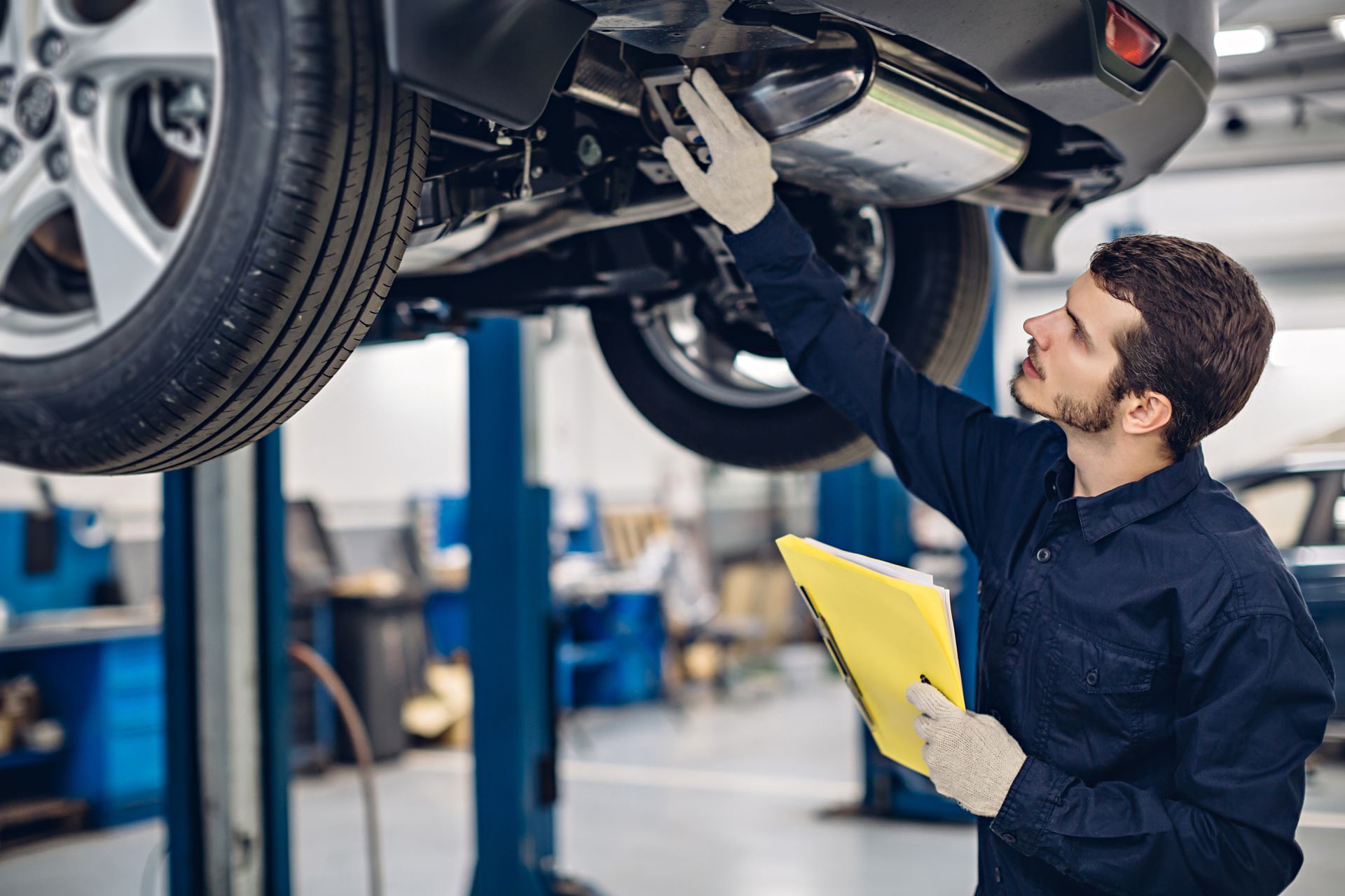 A mechanic is examining the underside of a car in a garage.