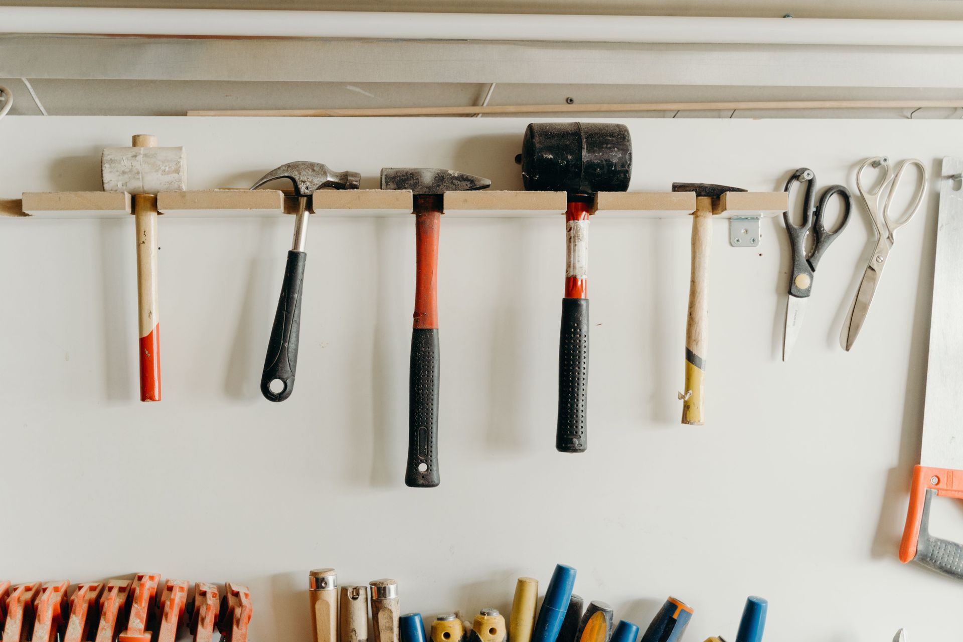 Tools hanging on a wall rack in a workshop, including hammers, pliers, and scissors.
