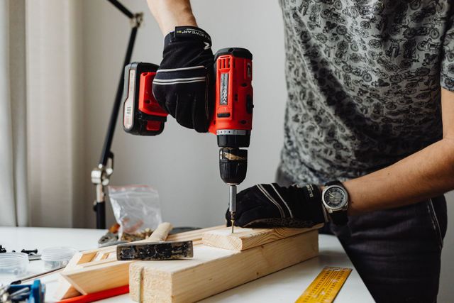 Person drilling a wooden plank on a workbench with a red cordless drill