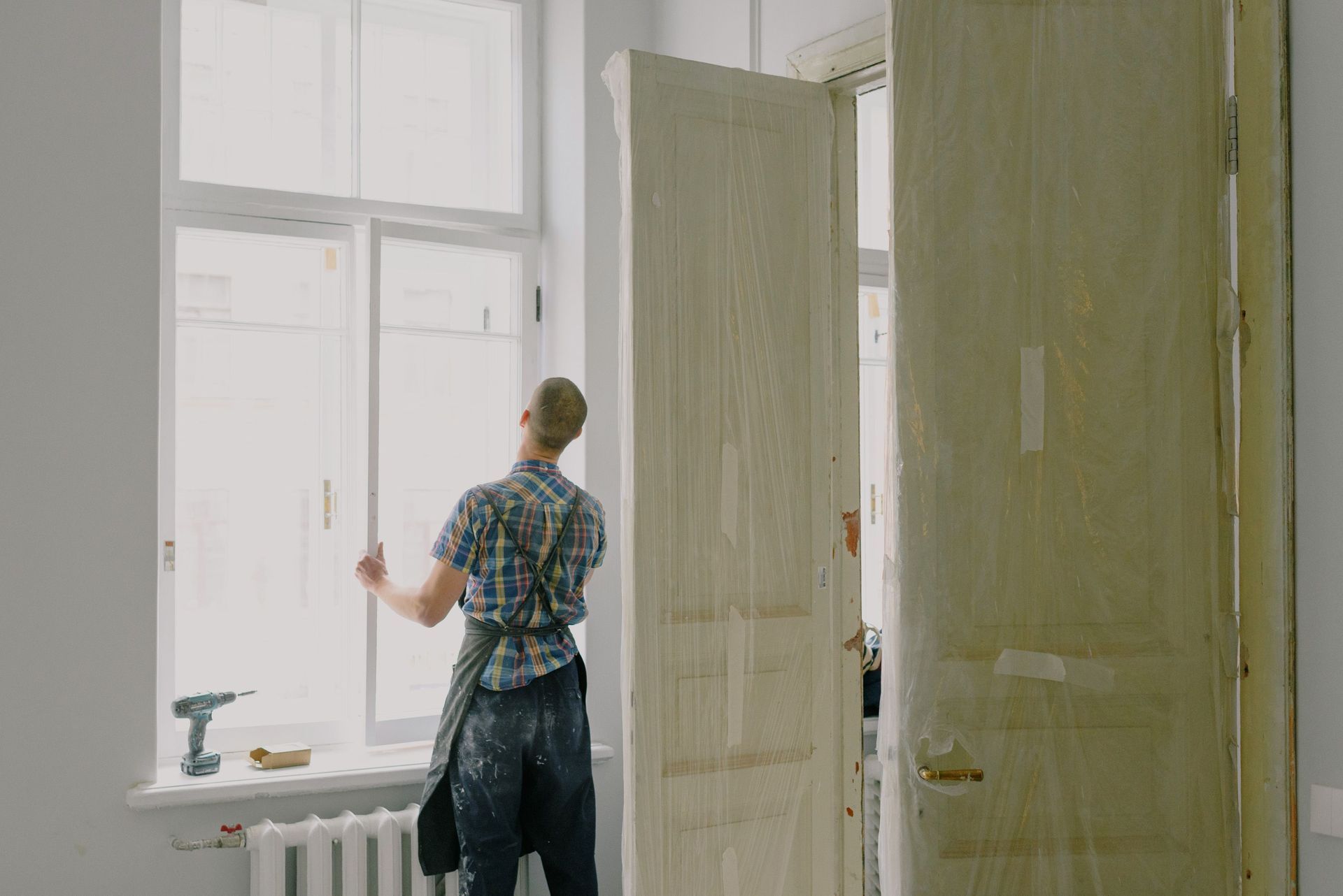 Person painting a white window frame in a bright room with large open panels