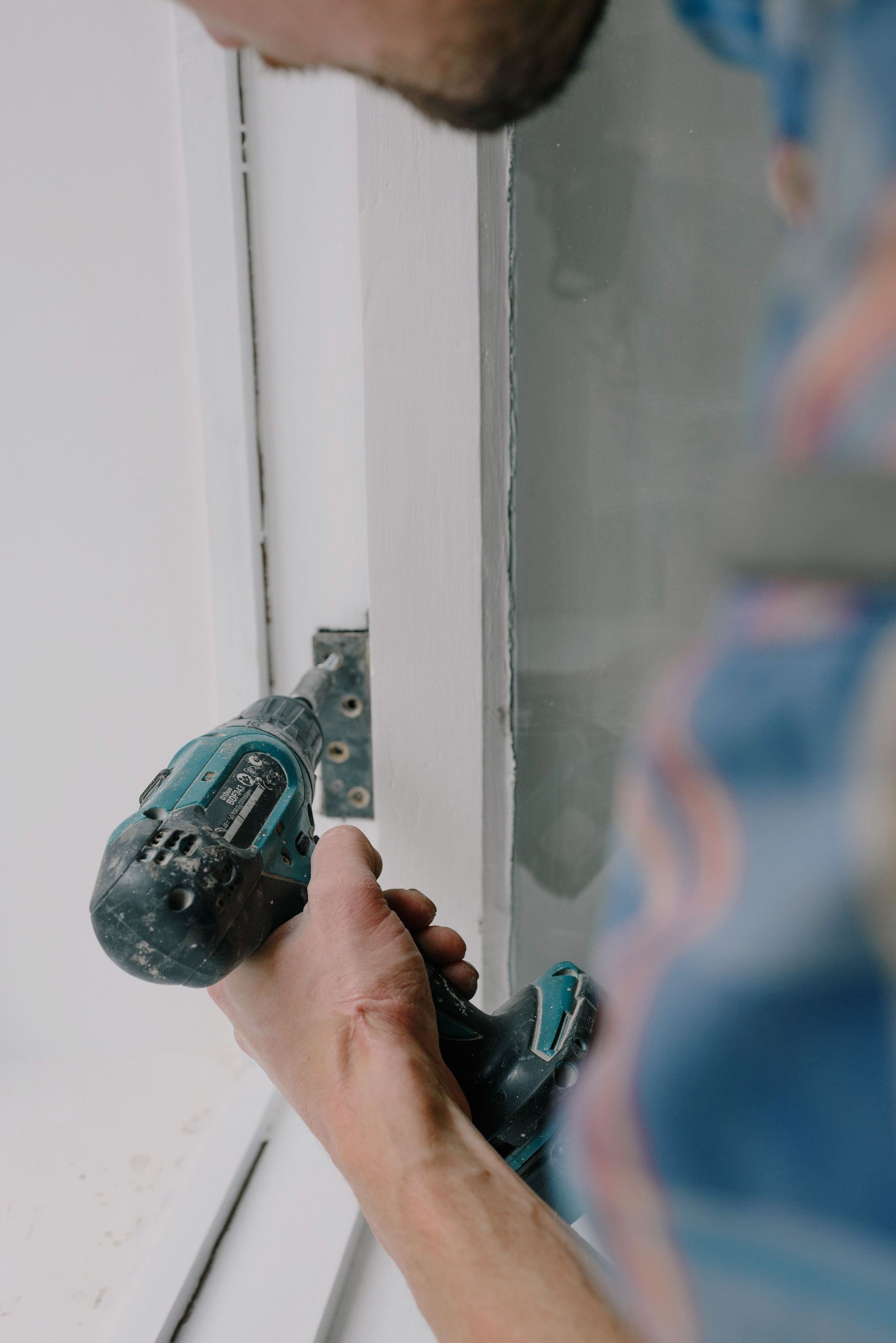 Person using a green drill to install a metal hinge on a white door frame