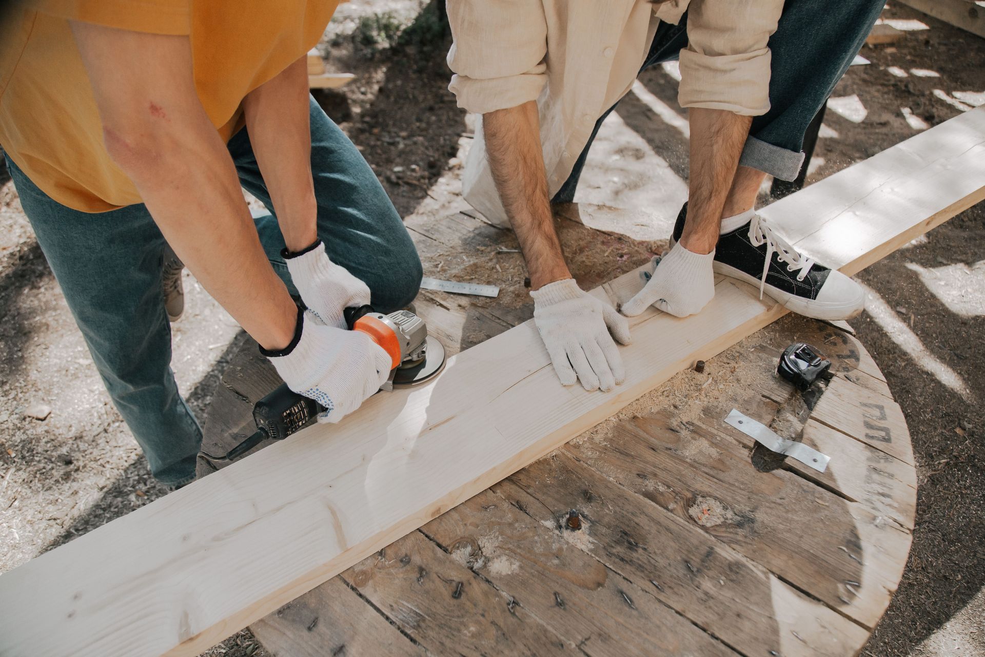 Three people in gloves painting a long white wooden beam on a worksite.