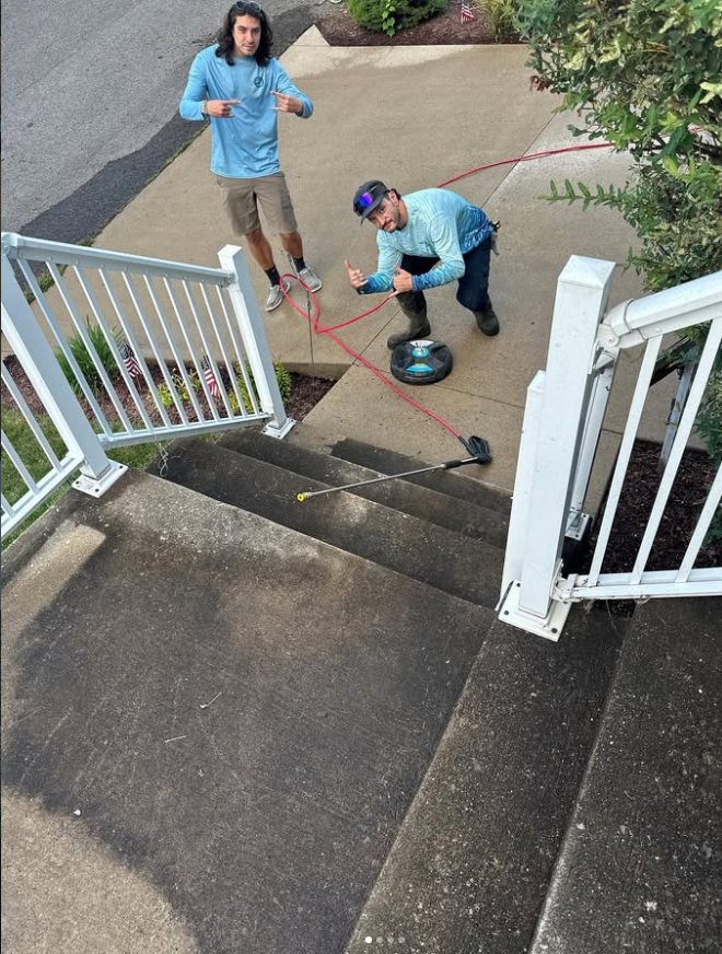 Two people cleaning a concrete stoop; one operates a floor buffer near a white porch railing.