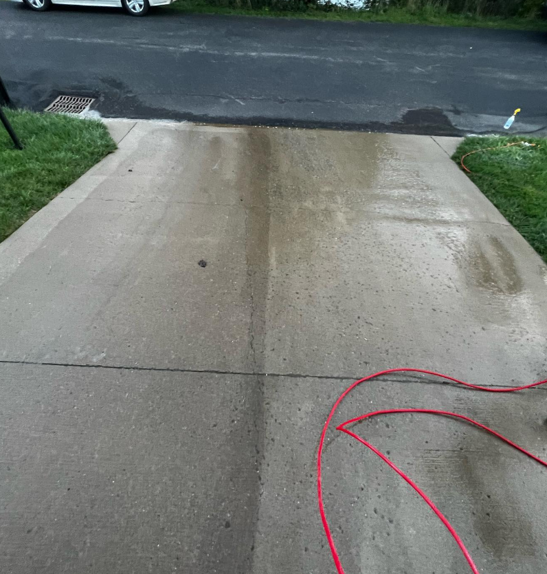 Wet concrete driveway leading to a street, with a red hose on the right side.