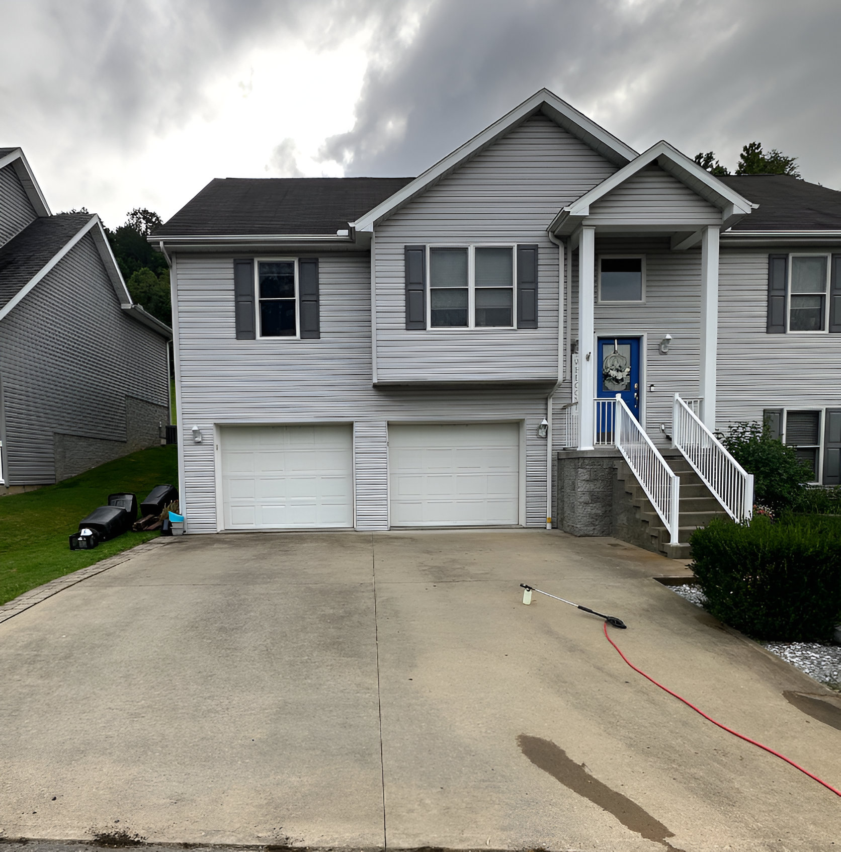 Suburban townhouse with two garage doors, white siding, and front steps under a cloudy sky